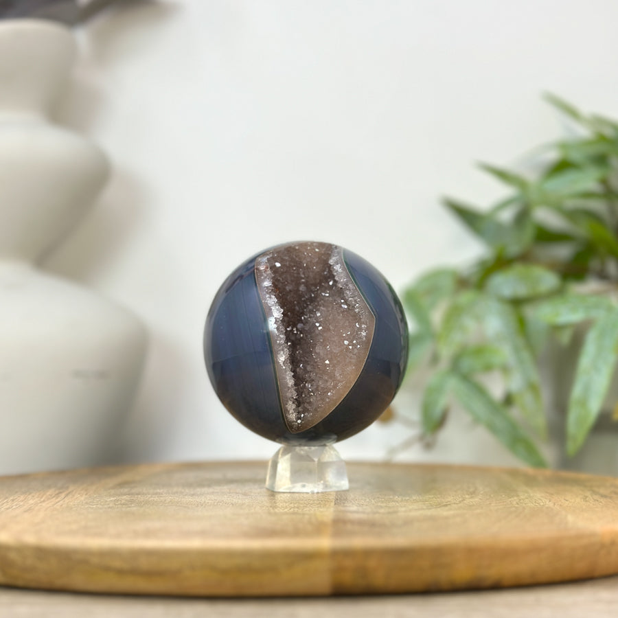 Echte Bänderachat-Sphäre aus Uruguay mit einer markant geöffneten, plastischen Druzy-Kristallkammer voller feiner, funkelnder Quarzspitzen.

