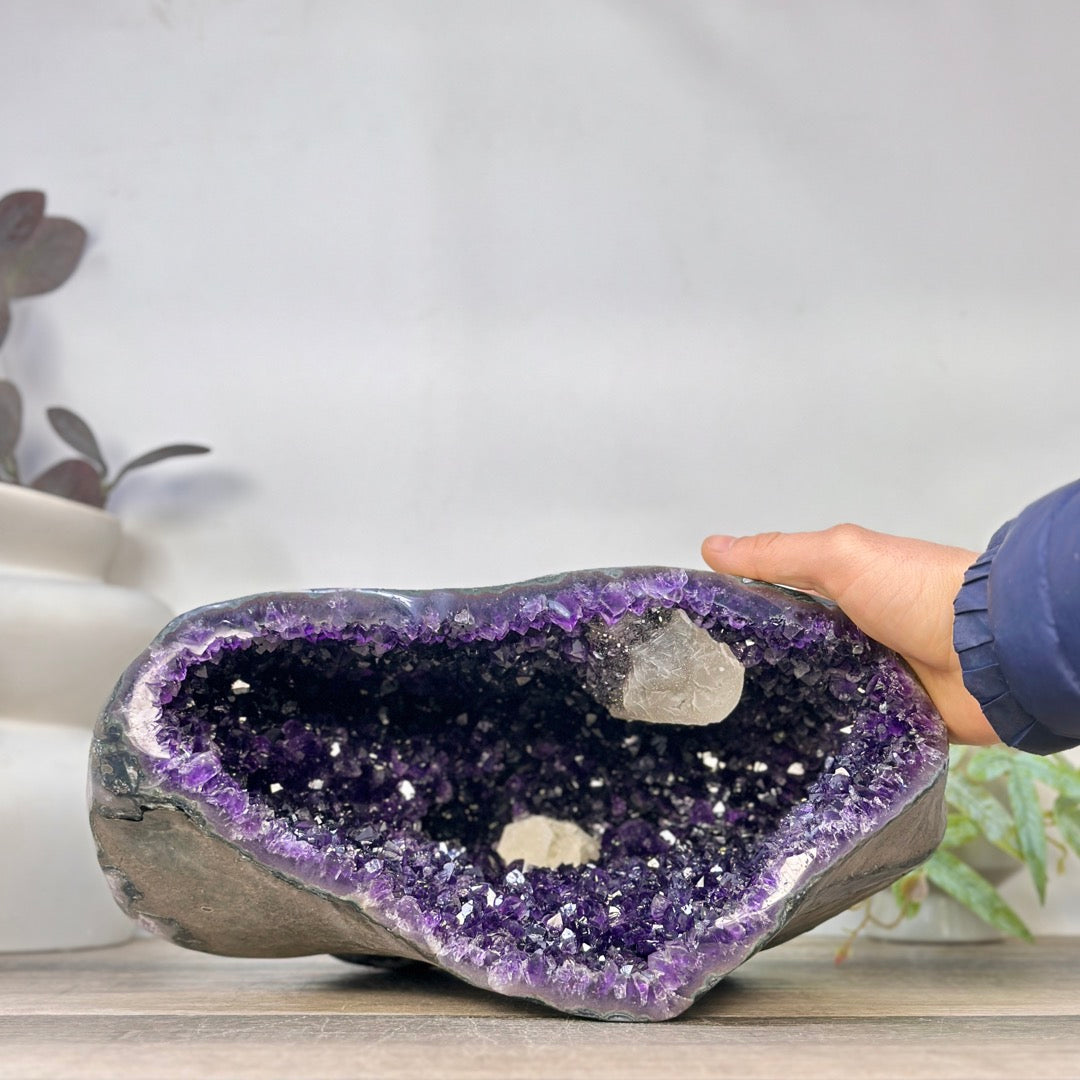 Eine Hand greift an die obere Kante der großen Amethyst-Geode, um die realen Proportionen und die Dimensionen der Kristallkammer zu demonstrieren.