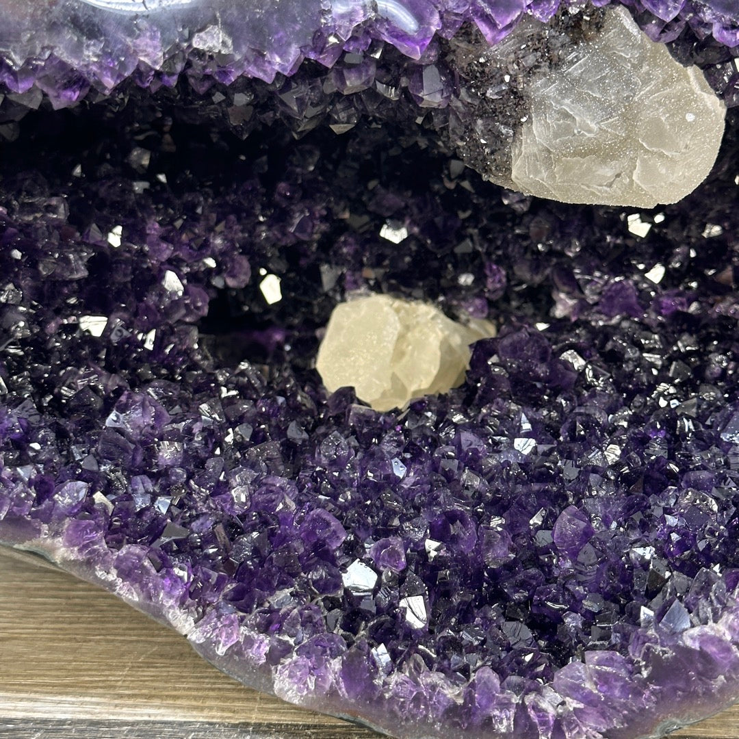 Schräge Seitenansicht der Amethyst-Skulptur, die die Tiefe der Kammer und den natürlich grauen Gesteinsmantel mit feinem Achatrand zeigt.
