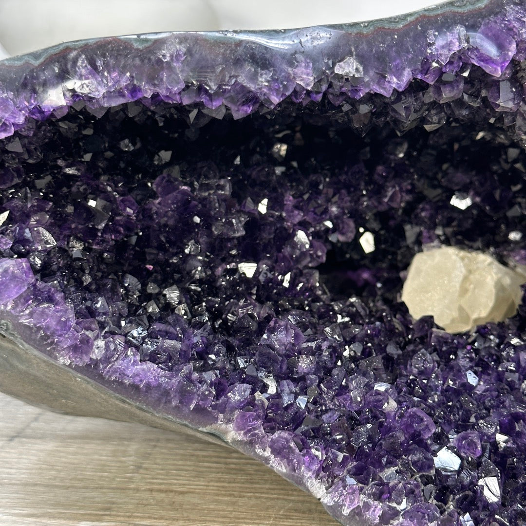 Makroaufnahme der funkelnden, dunkelvioletten Amethyst-Einzelkristalle im Inneren der Geode mit Blick auf ein quadratisches Kalzit-Mineral.