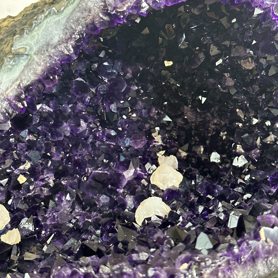 Schräge Profilansicht der Amethyst-Skulptur, welche die Tiefe der Kristallkammer sowie den glatt geschliffenen, grauen Gesteinsmantel zeigt.
