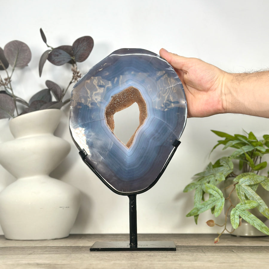 Eine Hand präsentiert das große, ovale blaue Achat-Kristallportal auf dem Ständer, um die echten Proportionen und die Höhe von 33,5 cm anschaulich zu demonstrieren.
