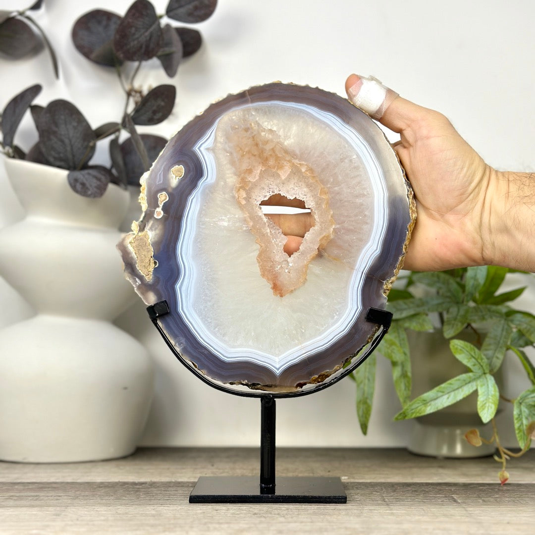 Eine Hand hält das blaue Achat-Quarz-Portal im Ständer, um die realen Proportionen und die beachtliche Gesamthöhe von 27 cm zu demonstrieren.
