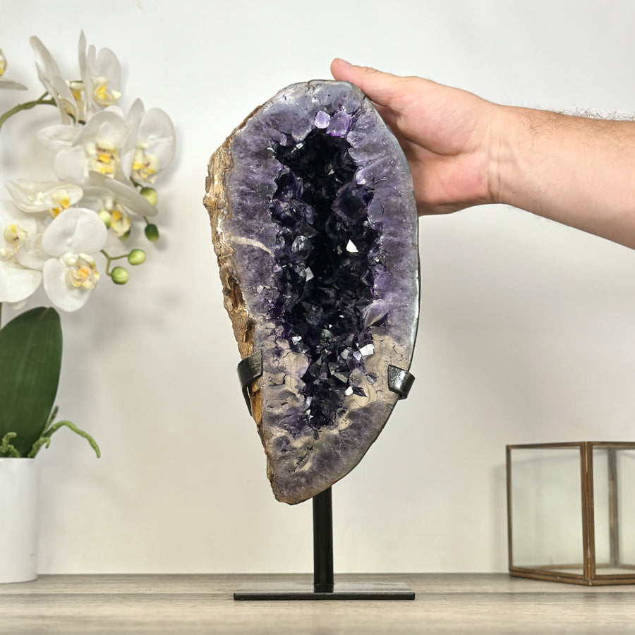 Eine Hand liegt seitlich an der schlanken Amethyst-Geode, um die imposante Höhe von 36 cm visuell zu verdeutlichen.