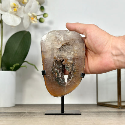 Eine Hand hält das Quarz-Portal mit den grünen Kristallen im Ständer, um die realen Dimensionen und die Gesamthöhe von 18 cm zu demonstrieren.

