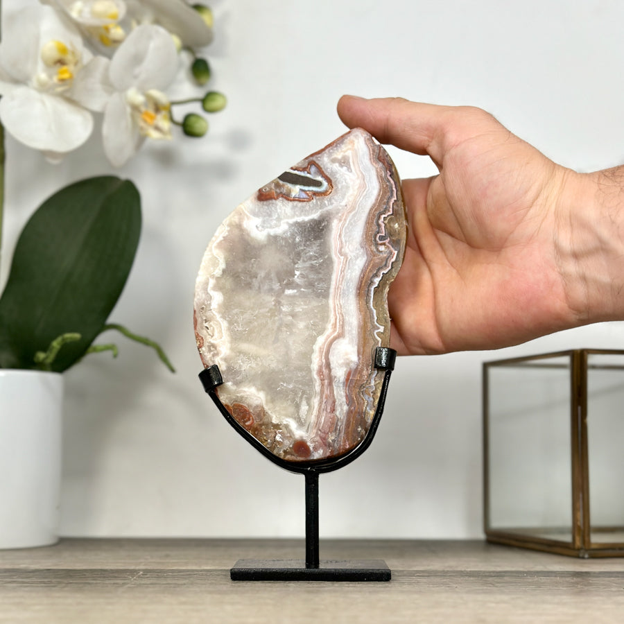 Eine Hand hält das Jaspis-Quarz-Portal im Design-Ständer, um die realen Proportionen und die Gesamthöhe von 20 cm zu demonstrieren.
