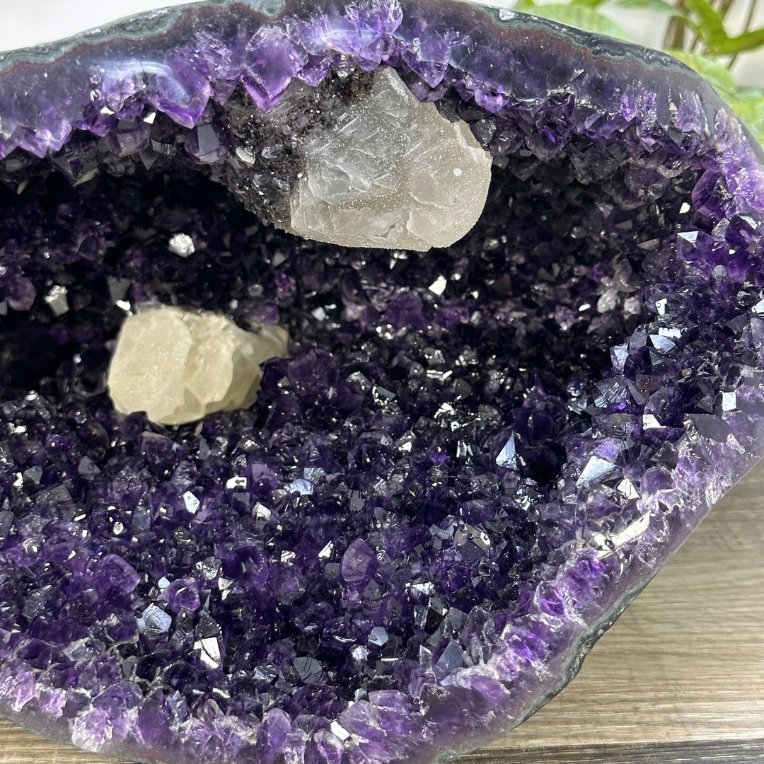 Detailansicht einer beigen, würfelförmigen Kalzit-Formation, umgeben von einem dichten Teppich aus violetten Amethyst-Kristallspitzen.
