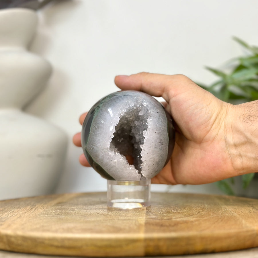 Eine Hand hält die runde Quarz-Kristallkugel, um die realen Proportionen und den Durchmesser von 8,9 cm anschaulich zu demonstrieren.
