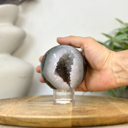 Eine Hand hält die runde Quarz-Kristallkugel, um die realen Proportionen und den Durchmesser von 8,9 cm anschaulich zu demonstrieren.
