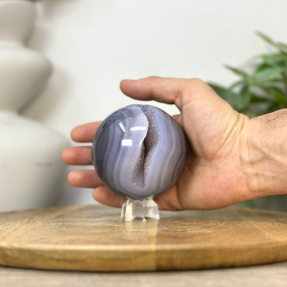 Eine Hand präsentiert die perfekt geschliffene Achat-Sphäre, um die echten Proportionen und den Durchmesser von 8 cm anschaulich zu demonstrieren.
