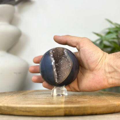Eine Hand präsentiert die handliche, perfekt geschliffene Achat-Kristallsphäre, um die echten Proportionen und den Durchmesser von 8 cm zu verdeutlichen.