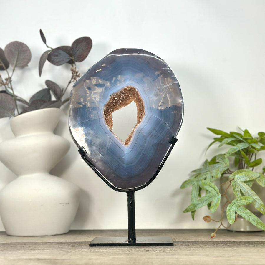 Großes ovales Kristall-Portal aus blauem Bänderachat und hellem Quarz aus Uruguay mit intensiv funkelnder Druzy-Oberfläche auf einem schwarzen Metallständer.