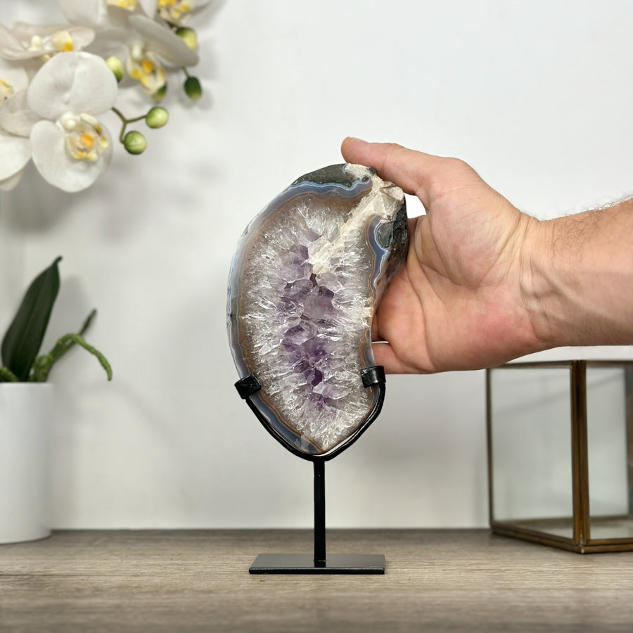 Eine Hand hält die Quarz- und Amethyst-Steinplatte auf dem Ständer, um die realen Proportionen und die Höhe von 21 cm zu demonstrieren.