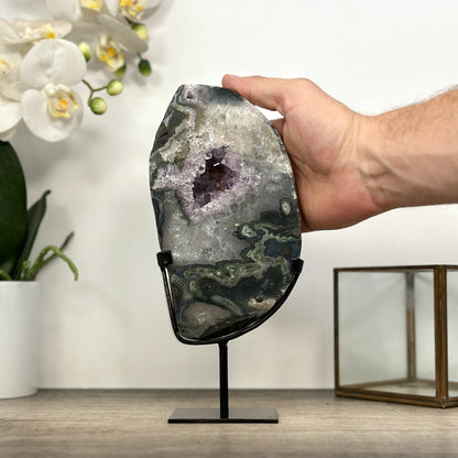 Eine Hand hält das Quarz-Geoden-Portal im Ständer, um die realen Dimensionen und die Gesamthöhe von 23,5 cm zu zeigen.