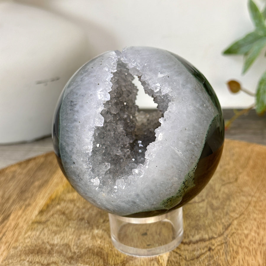 Schräge Seitenansicht der Naturstein-Sphäre, die die perfekte Symmetrie der Kugelform und die Tiefe der offenen Kristallhöhle abbildet.
