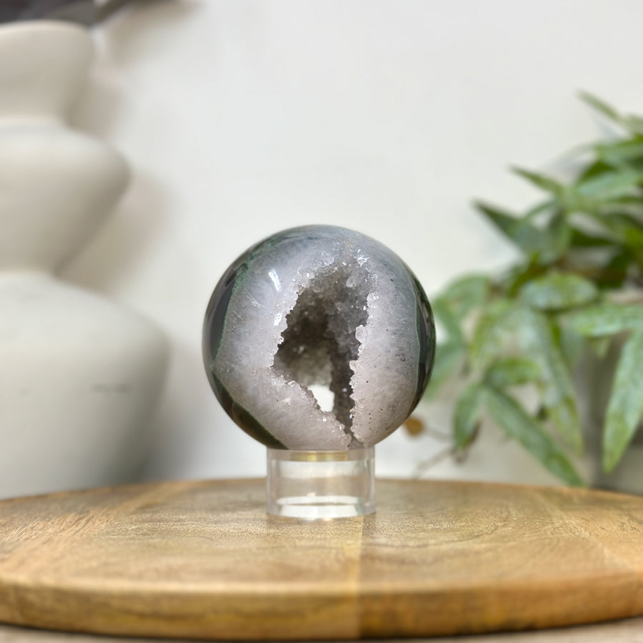 Präzise geschliffene Quarz-Sphäre aus Uruguay mit einer weit geöffneten Druzy-Kristallkammer und einer feinen, äußeren Bänderachat-Fassung.