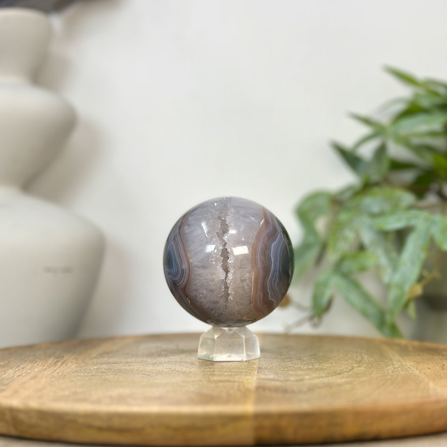 Echte Quarz-Sphäre aus Uruguay mit einer weit geöffneten Kristallkammer, einem lichtreflektierenden Druzy-Innenraum und feiner Bänderachat-Fassung.
