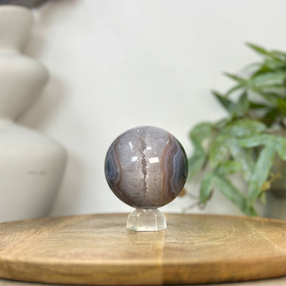 Echte Quarz-Sphäre aus Uruguay mit einer weit geöffneten Kristallkammer, einem lichtreflektierenden Druzy-Innenraum und feiner Bänderachat-Fassung.
